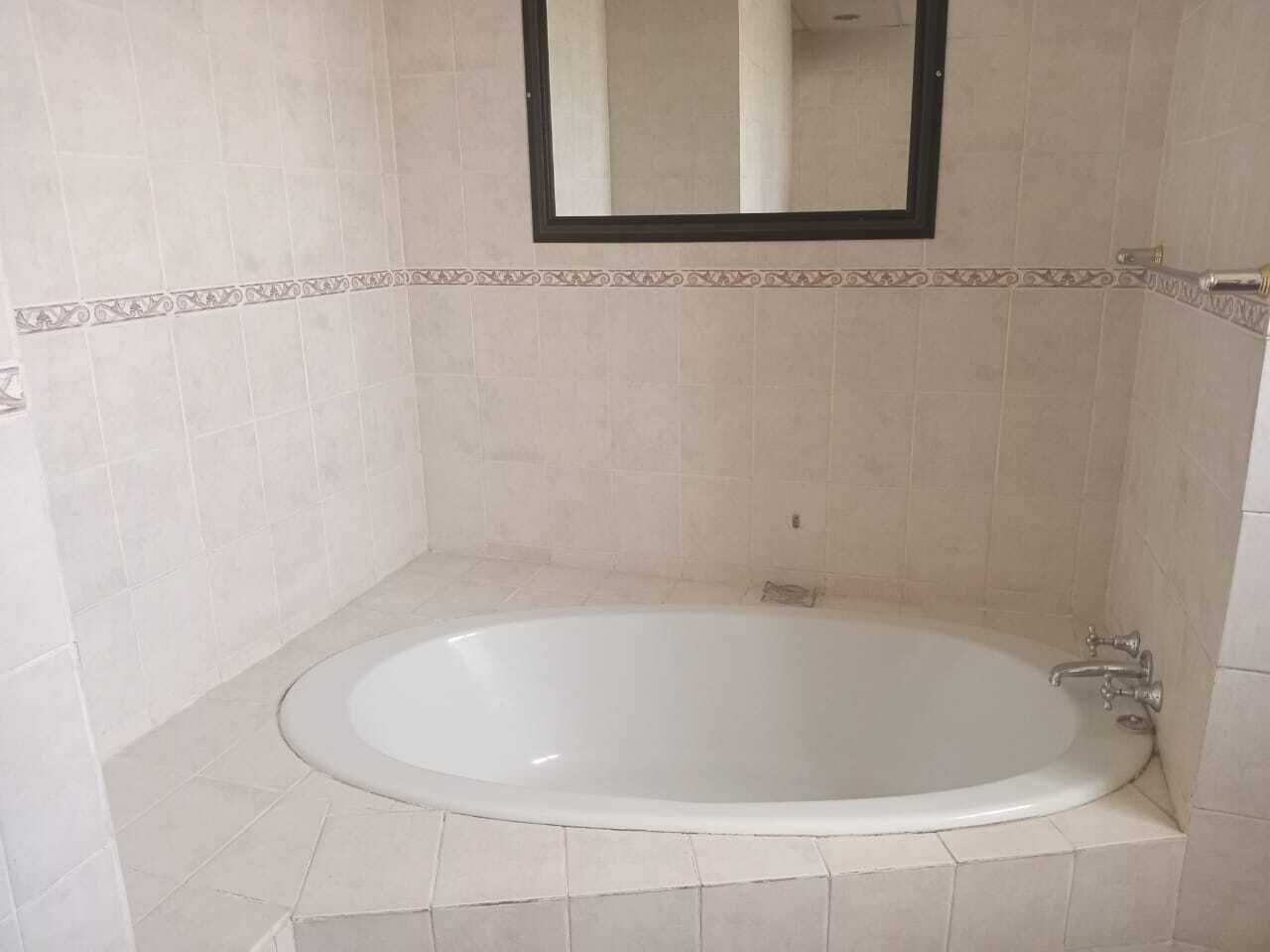 Een badkamer met een vrijstaand bad, een spiegel erboven en decoratieve tegelranden.