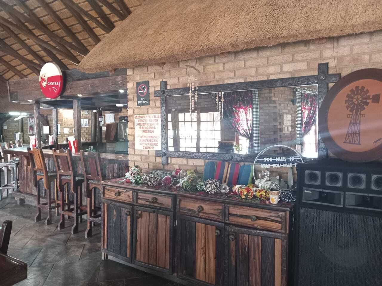 Un área de bar rústica con muebles de madera, techo de paja y decoración con molino.