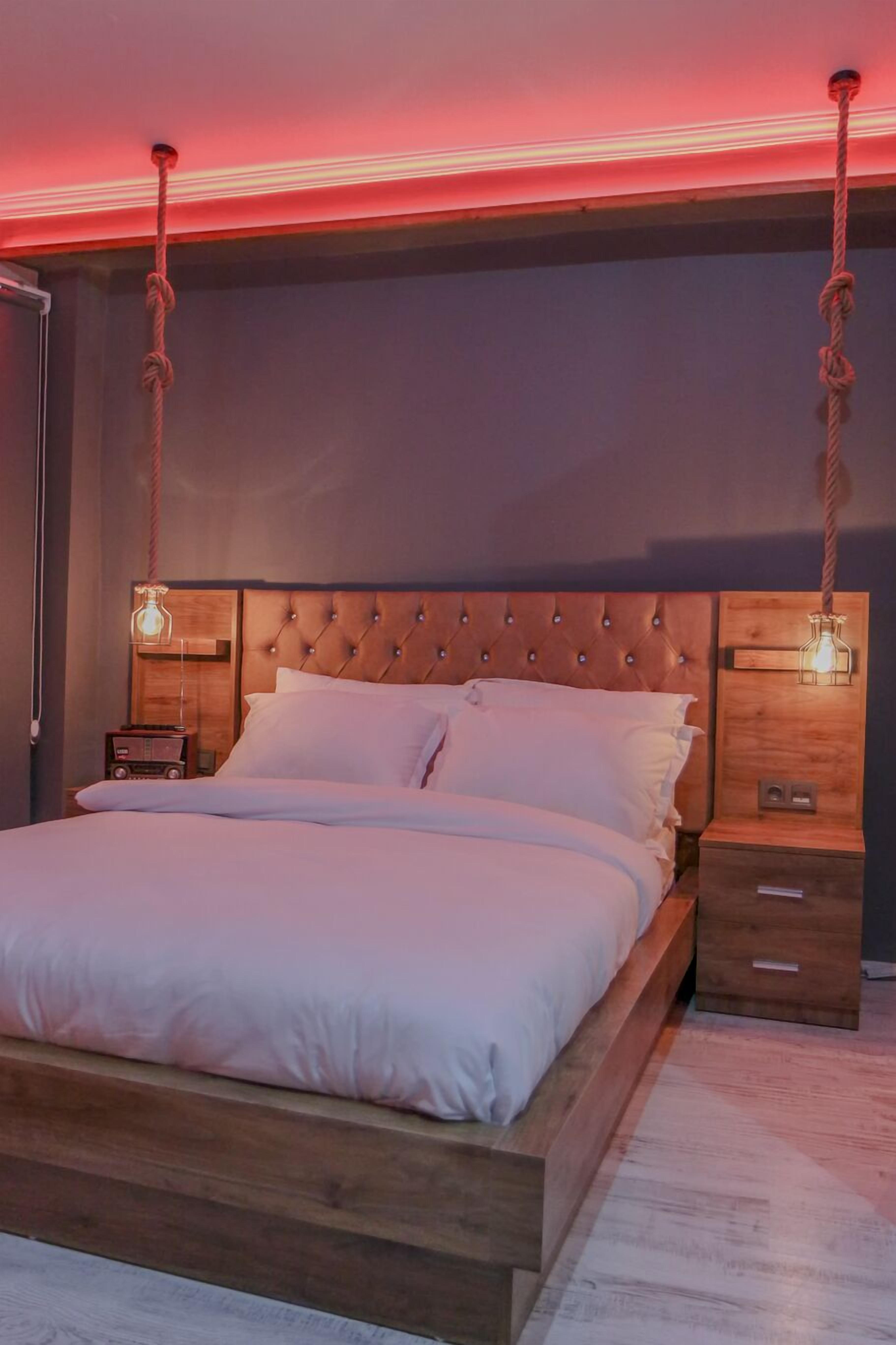 A bedroom with a wooden headboard, a bed with white bedding, two bedside tables with lamps, and a hanging rope decoration.