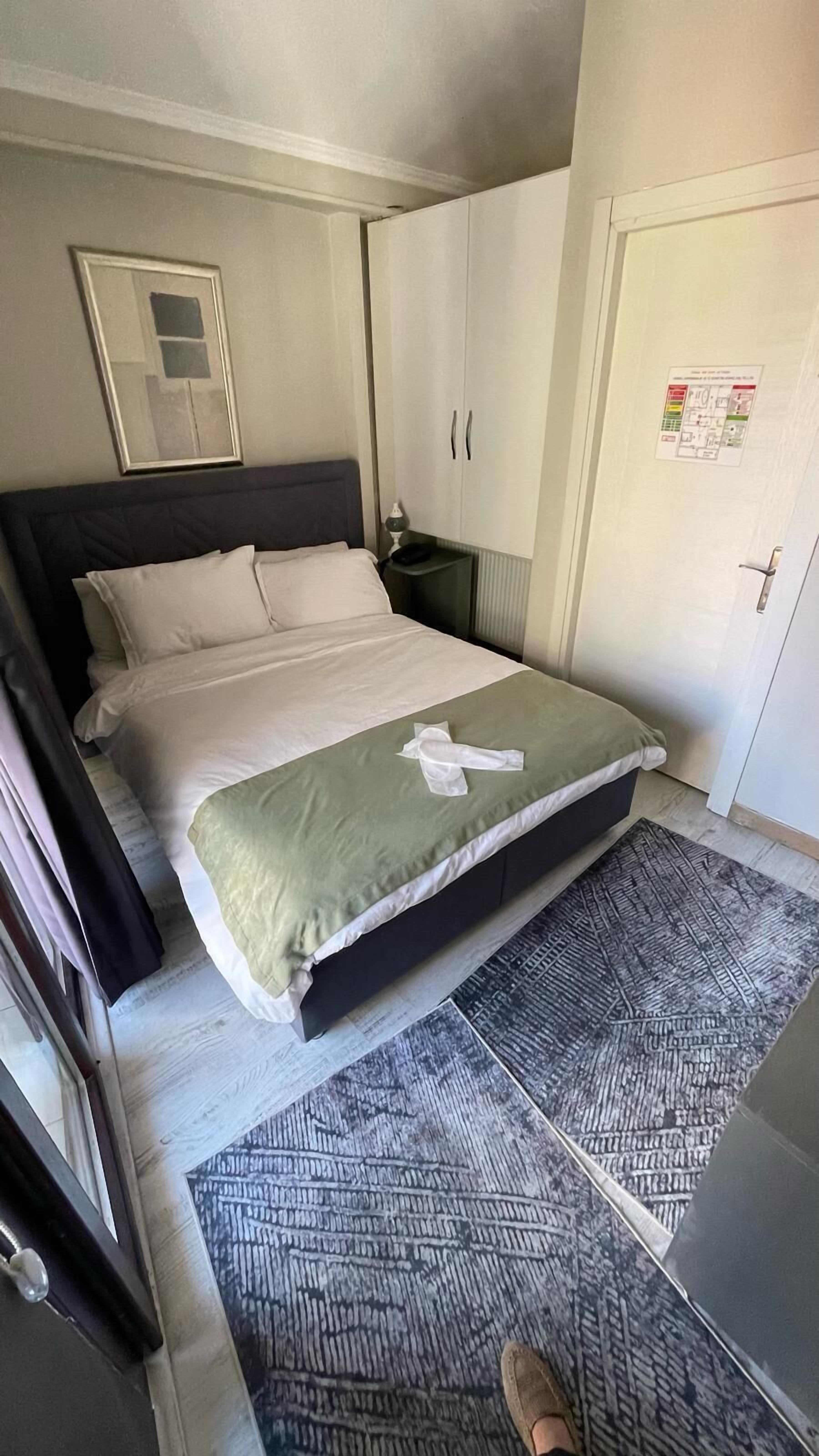 A neatly made bed with a green blanket, a bedside table with a lamp, and a door with a fire safety poster.