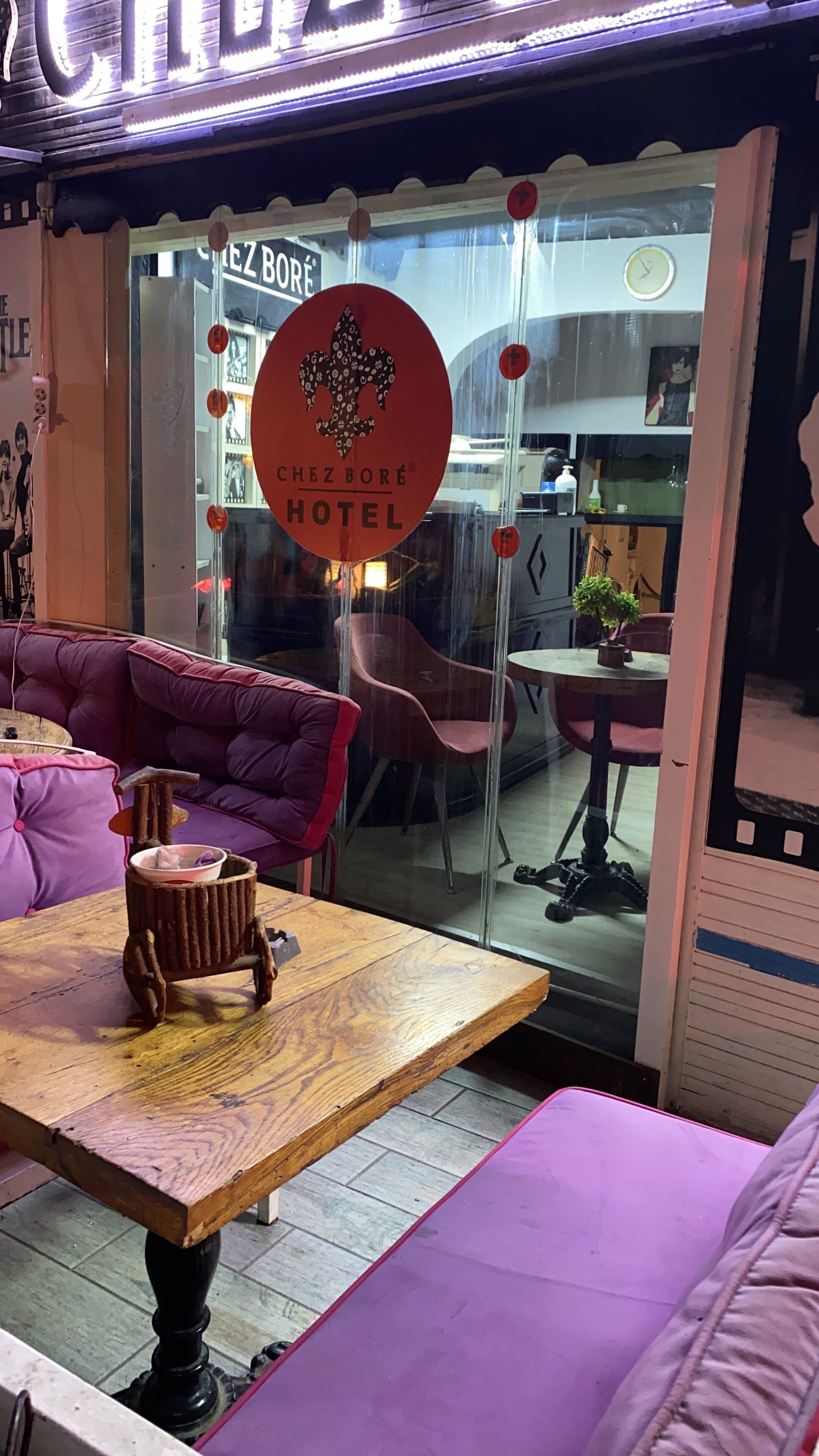 A cozy interior with a wooden table, purple seating, and a glass door with a sign for 'CHEZ BORE HOTEL'.