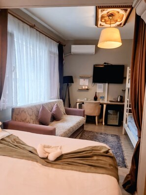 A hotel room with a bed, a sofa, a desk, a television, and an air conditioning unit. - Chez Bore  (Istanbul)