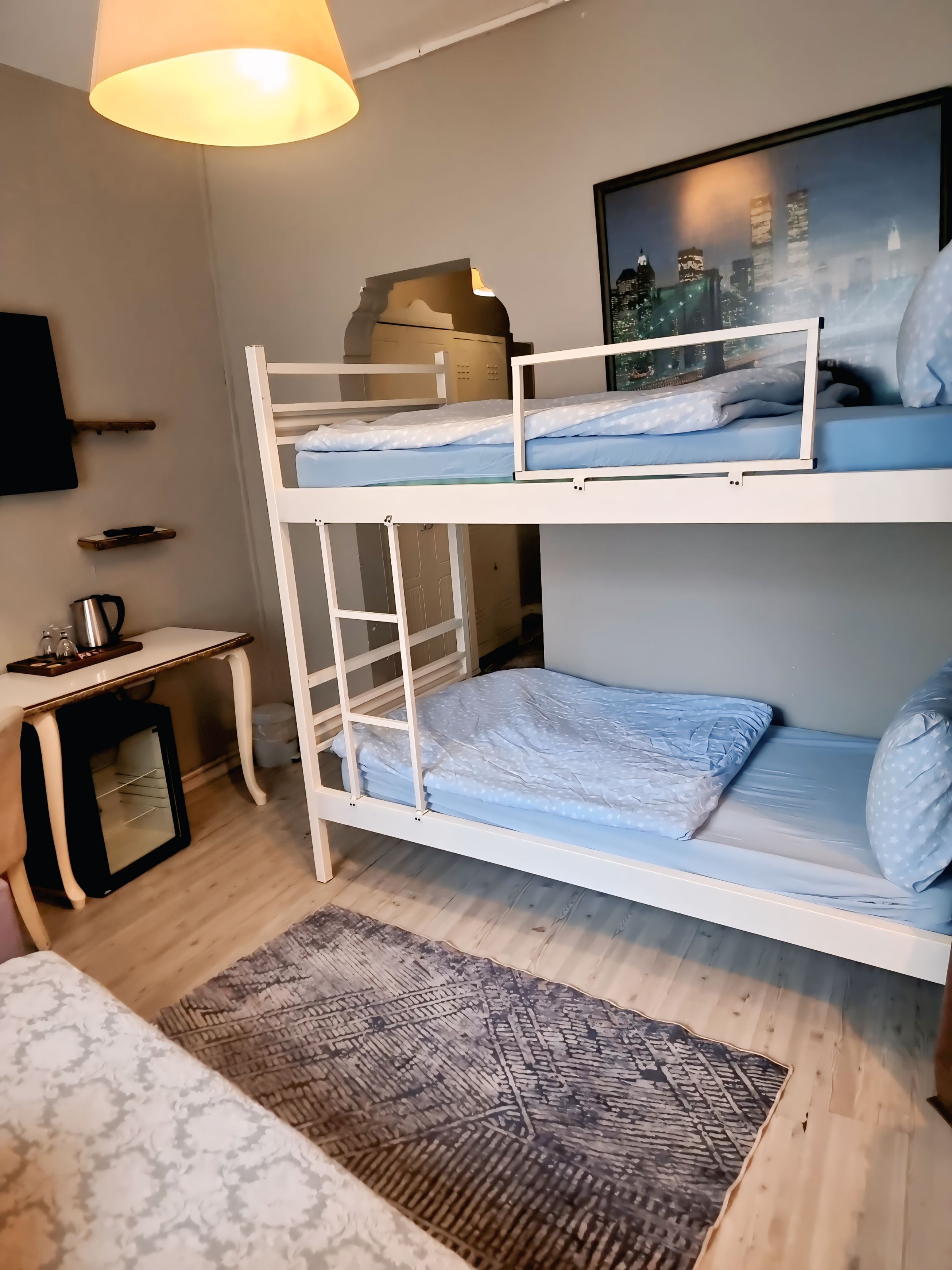 A bunk bed room with a cityscape view, a small desk with a lamp, and a patterned rug.