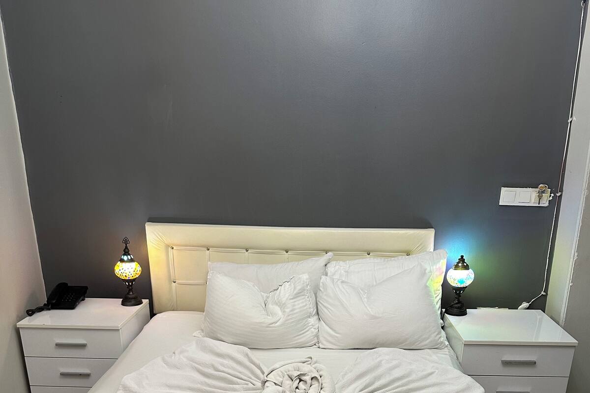 A neatly made bed with a towel art centerpiece, white bedding, and two bedside lamps.