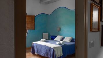 Un dormitorio con cabecera azul, una cama con ropa blanca, una mesita de noche y una lámpara de pared.