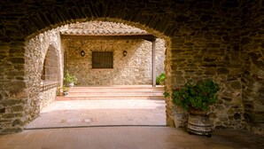 An arched stone doorway leading into a courtyard with steps, a potted plant, and a wall-mounted light fixture.