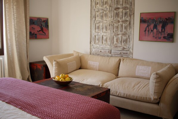 A cozy room with a beige sofa, a wooden table with a bowl of fruit, and artwork on the walls.