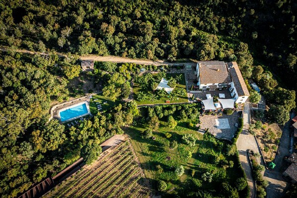 An aerial view of a property with a swimming pool, a large house, and surrounding gardens.