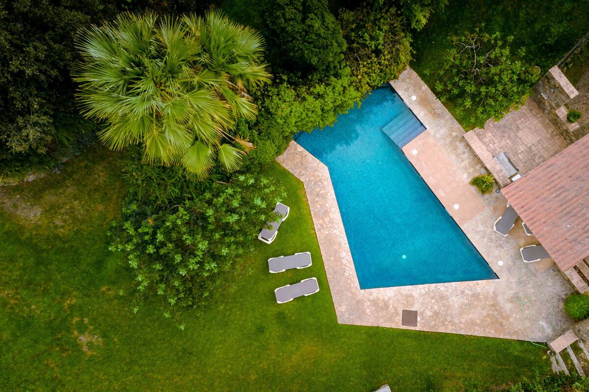 An aerial view of a swimming pool surrounded by a stone deck, with a few lounge chairs and a small table.