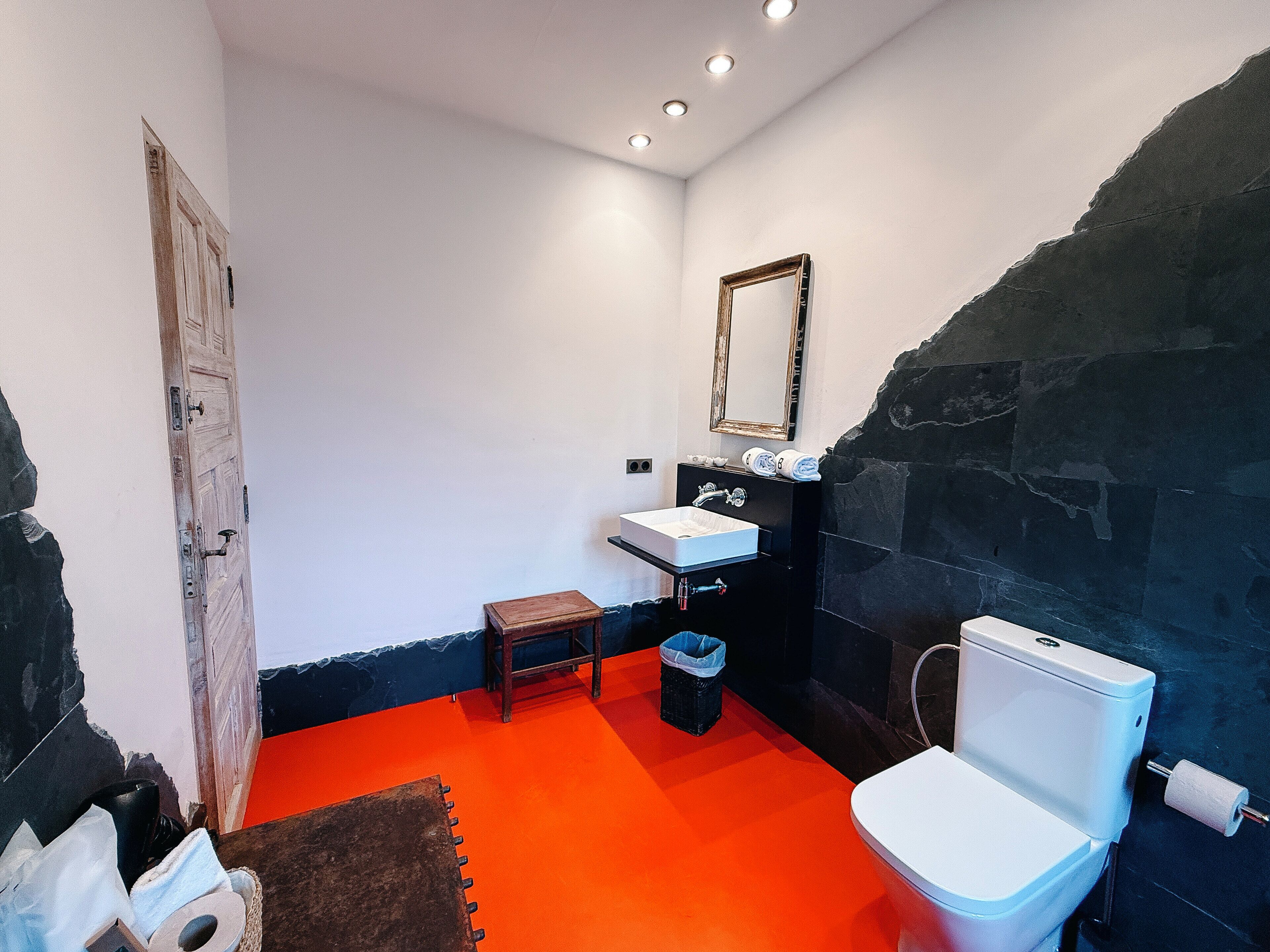 A bathroom with a white sink, a mirror, a toilet, and a red floor.