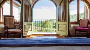 A room with a balcony, two chairs, and a view of a green landscape.