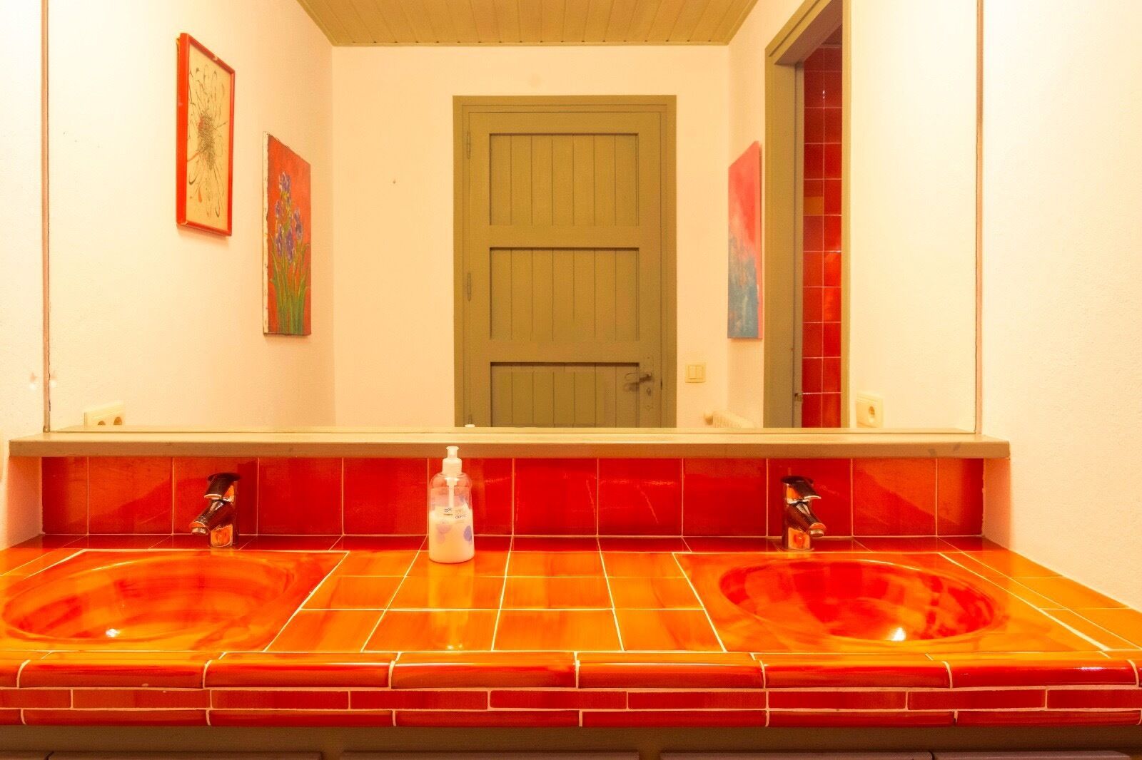 A bathroom with two sinks, red-tiled walls, and a green door.