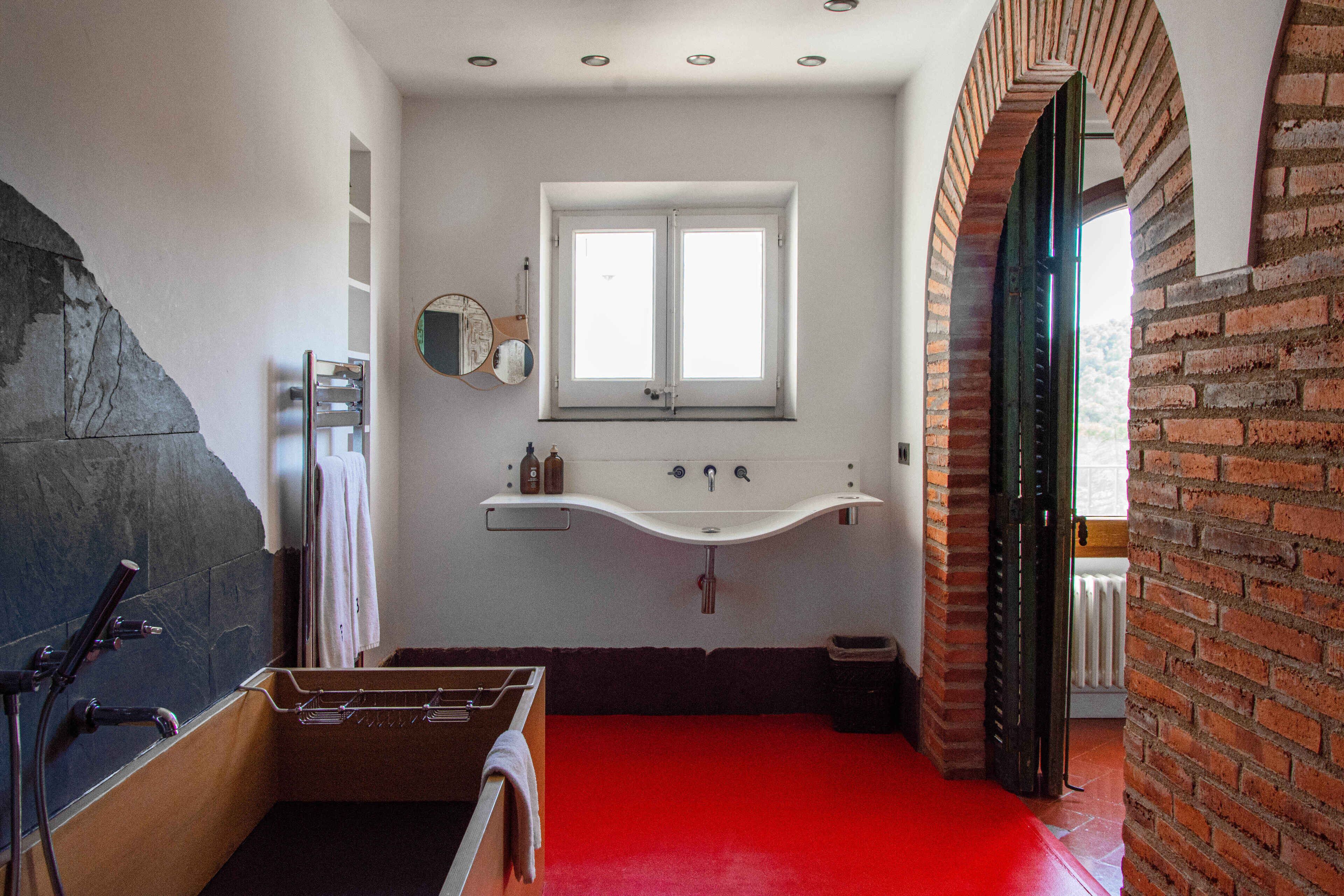 A bathroom with a stone wall, a white sink, a mirror, and a red floor.