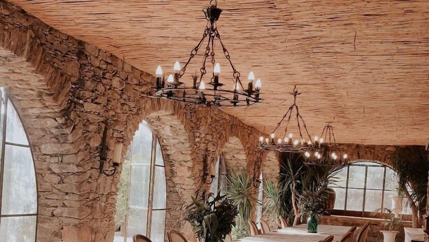 A long dining table with chairs, a chandelier, and stone walls.