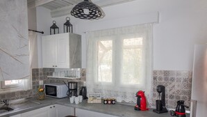A kitchen with white cabinets, a microwave, a coffee maker, and wooden stools. - Galini Apartment (Rhodes)