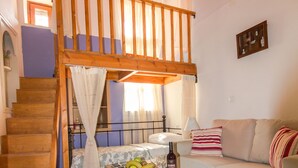 A cozy living room with a wooden staircase, a sofa, a coffee table with fruits and a bottle, and a small table with a lamp. - Galini Apartment (Rhodes)