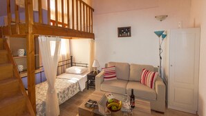 A cozy room with a wooden staircase, a bed with a canopy, a sofa, a small table with fruits and glasses, and a lamp. - Galini Apartment (Rhodes)
