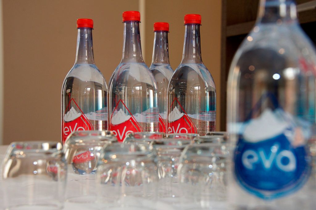 Cuatro botellas de vidrio transparente con tapas rojas y una botella azul con tapa roja, sobre una mesa.