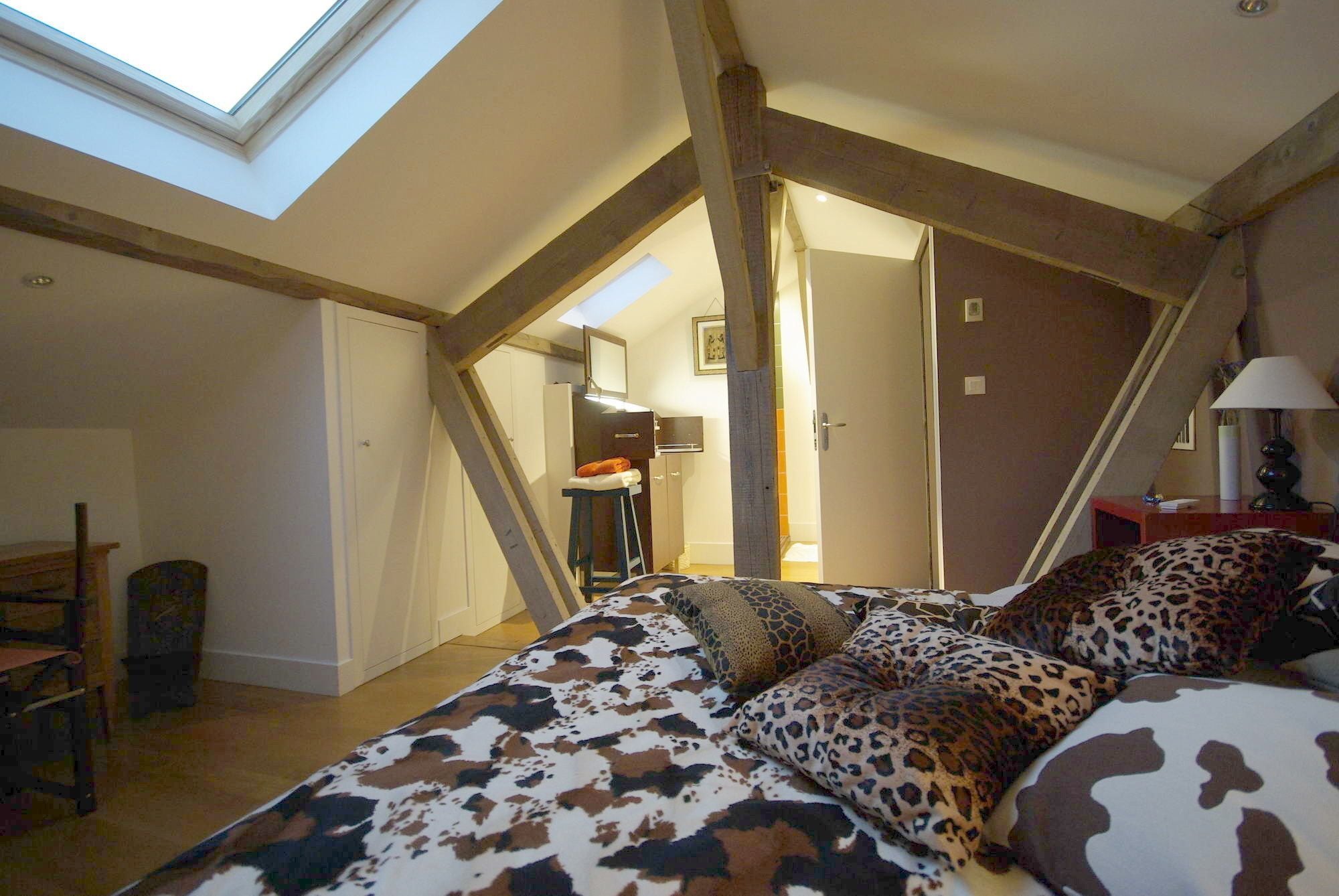 A bedroom with a sloped ceiling, a bed with a cow print cover, a desk, and a chair.