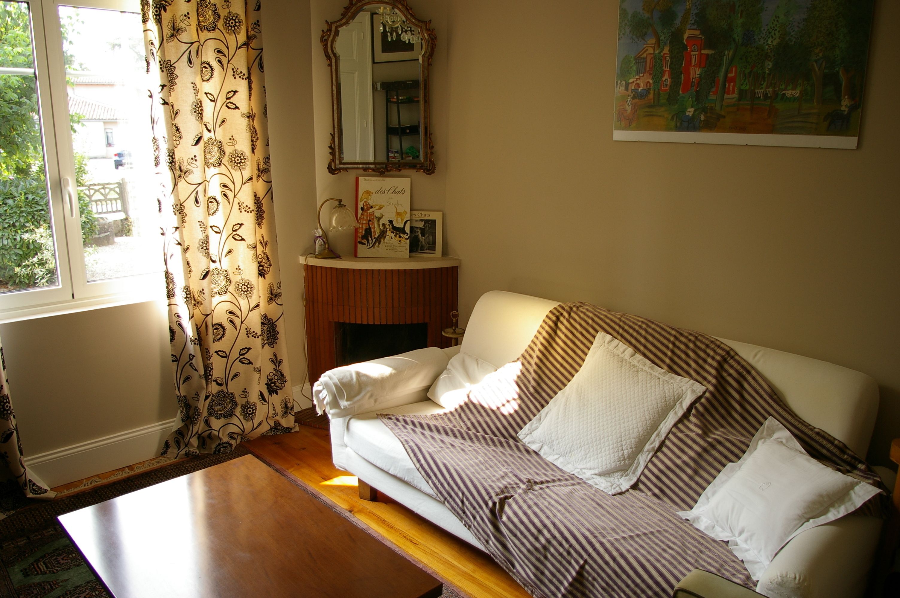 A living room with a white sofa, a wooden coffee table, a patterned curtain, a mirror, and a painting on the wall.