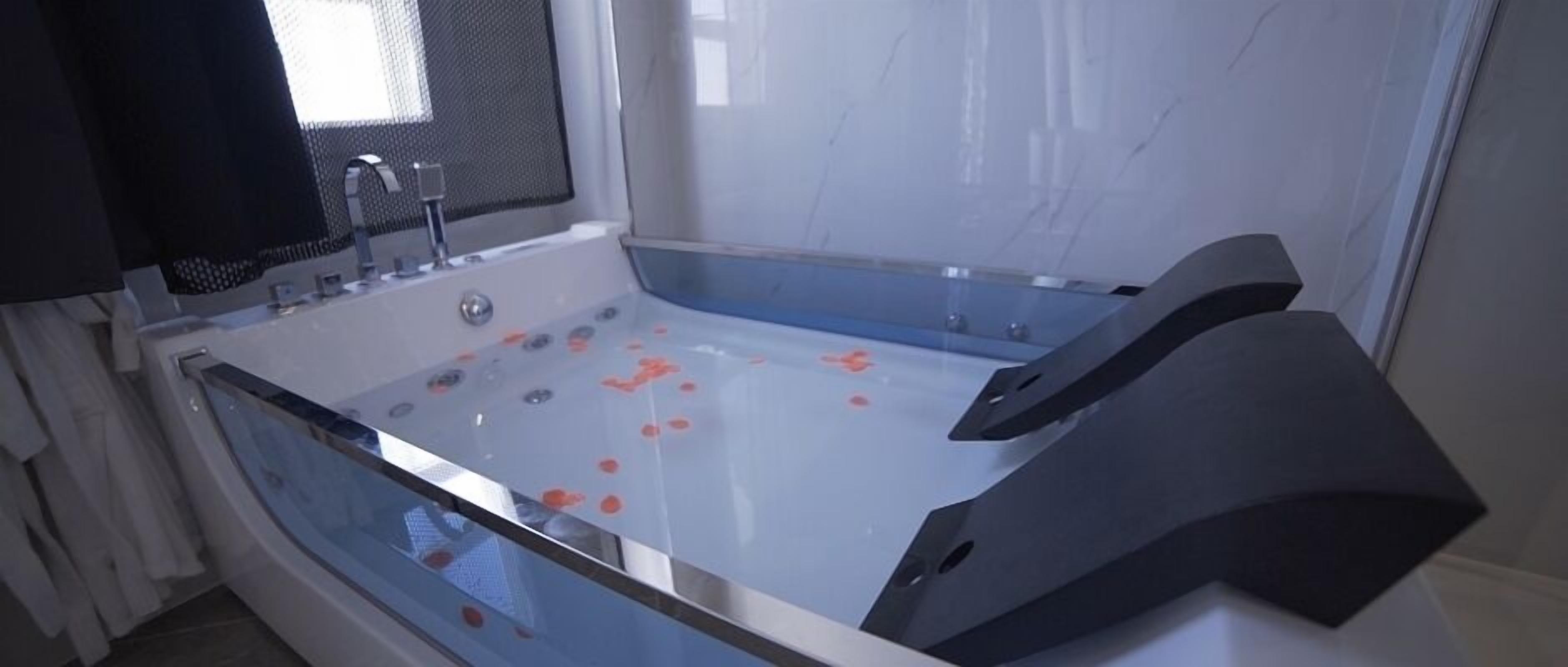 A modern bathroom with a large bathtub, a shower area, and a window with a mesh screen.