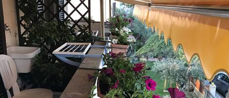 A covered outdoor seating area with a long table, chairs, and potted plants.