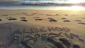 Huellas en la playa con la inscripción "ALBERGO RISPECIA" escrita en la arena.