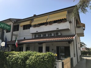 Un edificio de dos pisos con techo de tejas, unidades de aire acondicionado y un balcón con plantas en macetas.