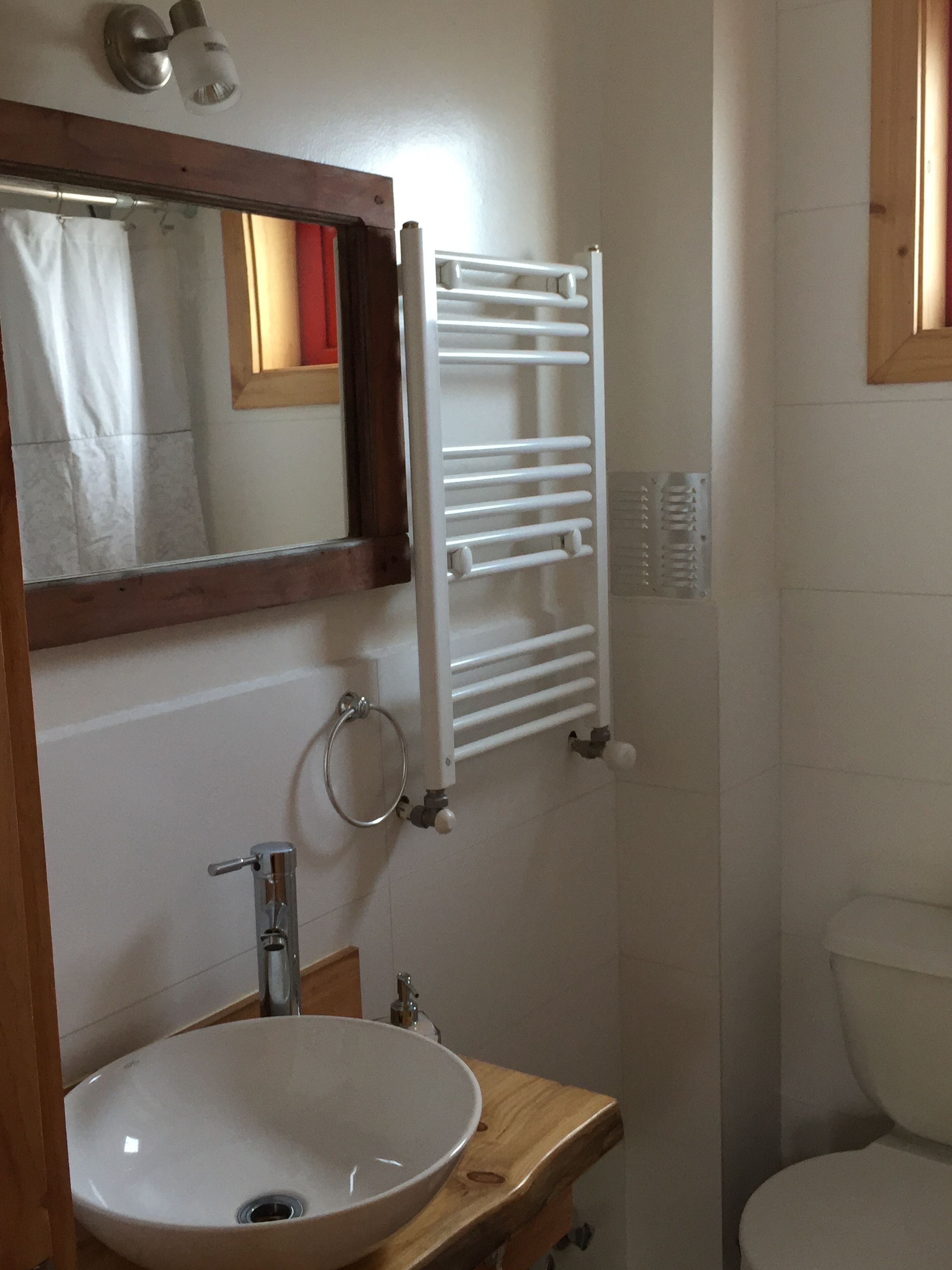 A bathroom with a wooden vanity, a white sink, a mirror, a towel rack, and a toilet.