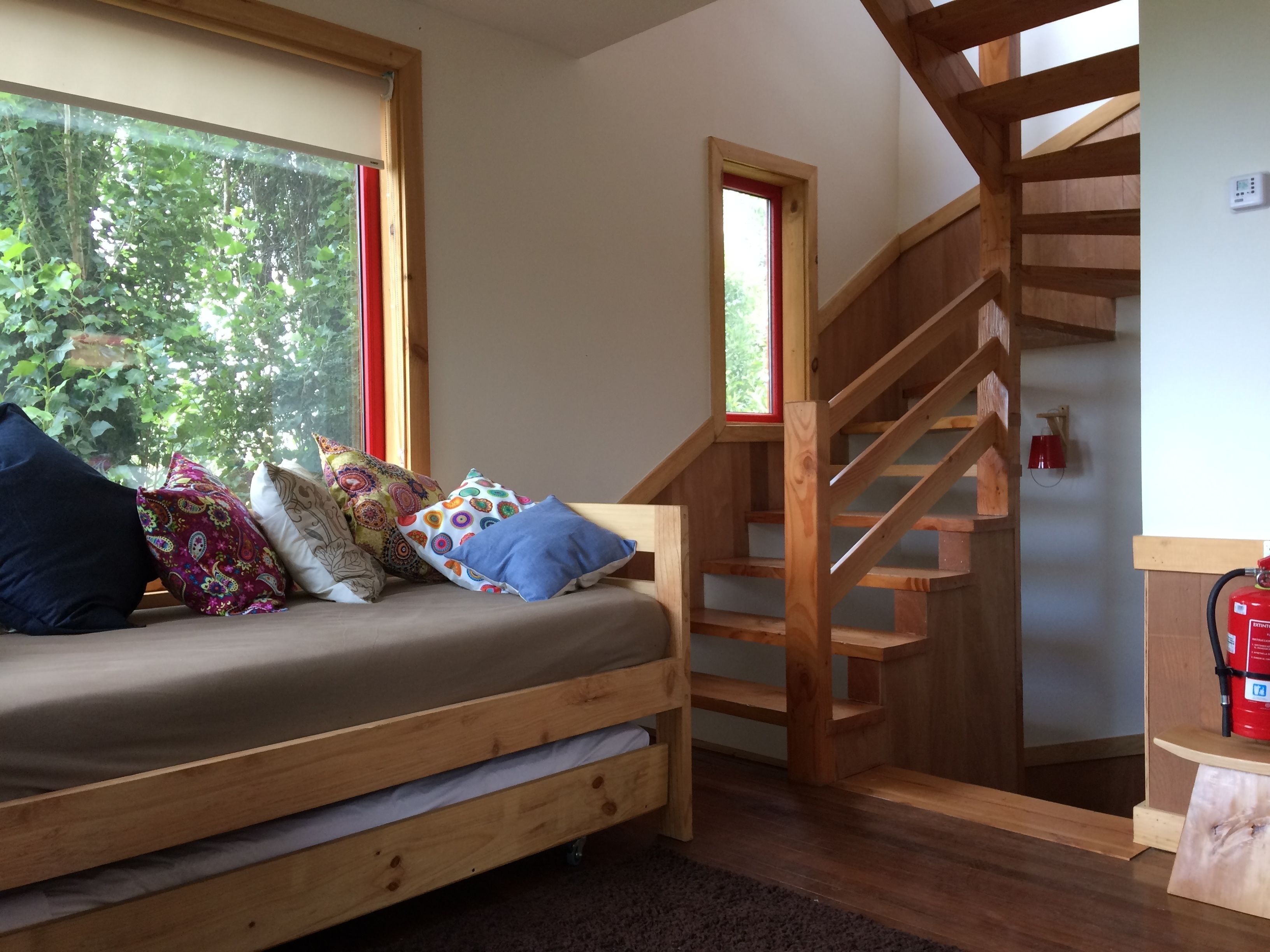 Una cama de madera con cajones para guardar cosas, una escalera de madera y una ventana con vistas al verdor.