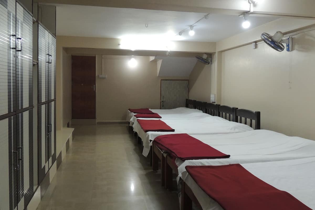 Ein Hotelzimmer mit mehreren nebeneinanderliegenden Betten, einem Deckenventilator und einer Tür zu einem weiteren Raum.