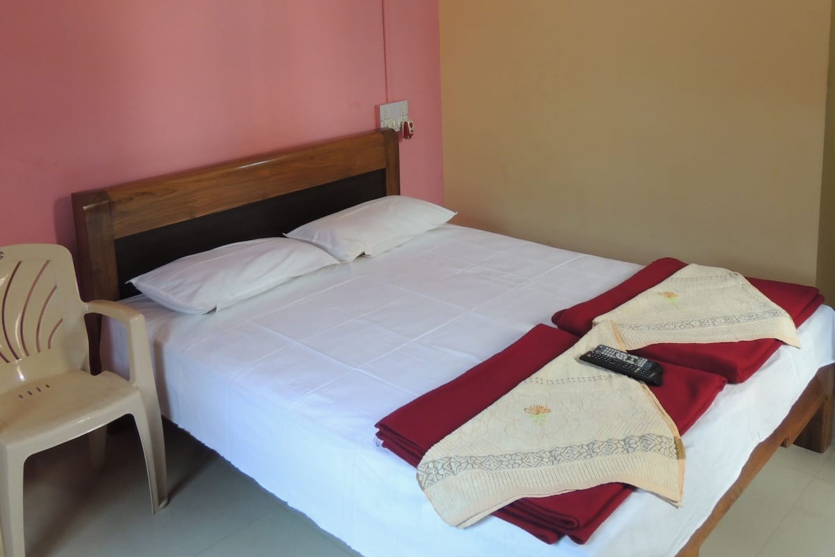 Ein Bett mit weißer Bettwäsche, einem hölzernen Kopfteil, einer roten Decke und einer Fernbedienung auf dem Bett.