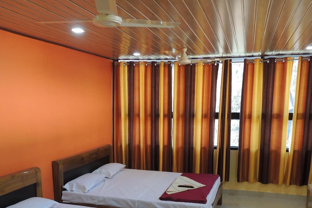 Ein Hotelzimmer mit zwei Betten, Holz-Kopfteilen, orangefarbenen Wänden, einem Deckenventilator und Vorhängen.