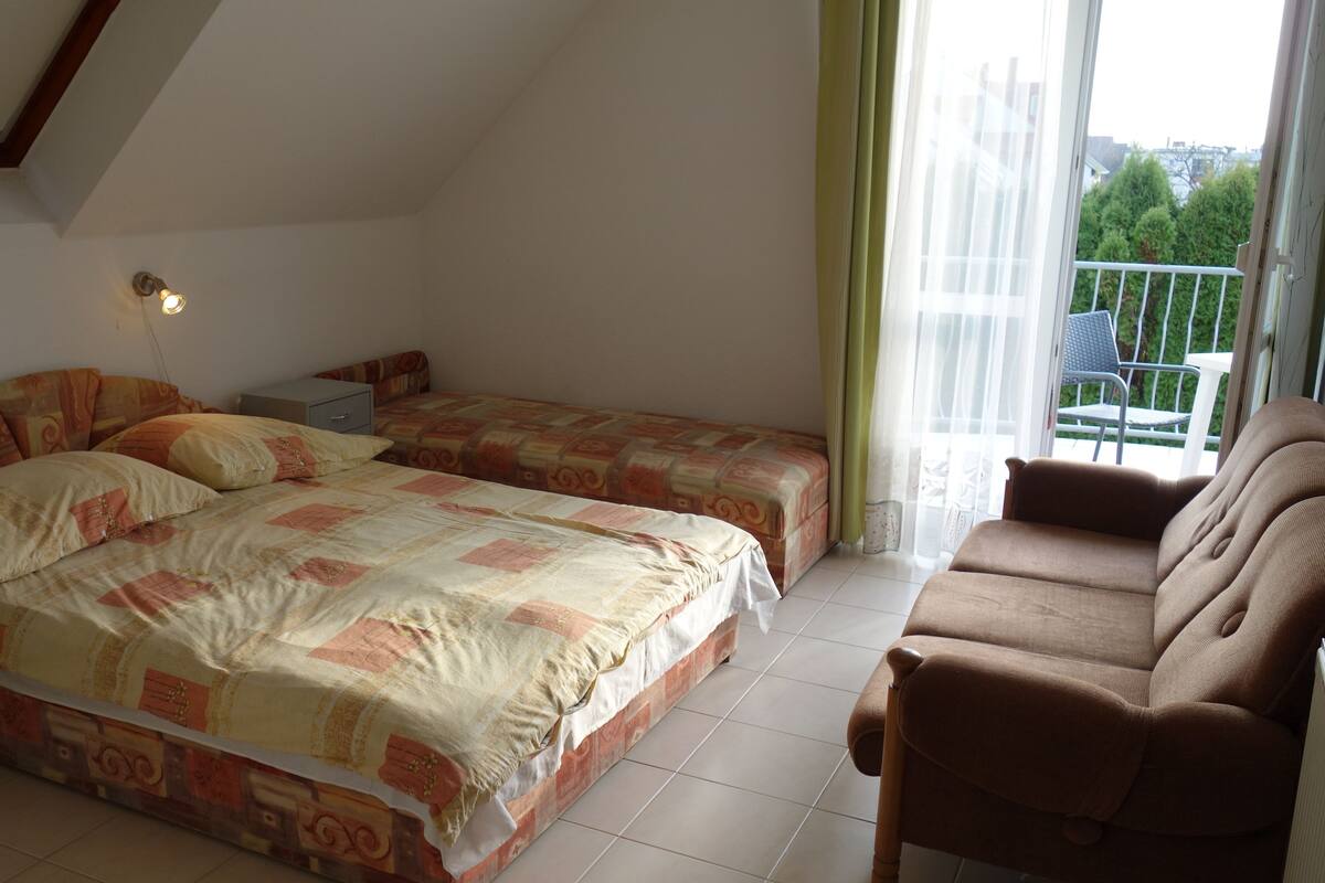 A bedroom with two beds, a chair, a table, and a balcony with a view.