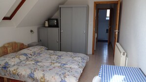 Een slaapkamer met een bed, een kast, een tafeltje en een deur naar een andere kamer.