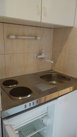 A compact kitchen with a stainless steel stove, a sink, and a built-in refrigerator. - Klassz Apartmanház (Balatonfured)