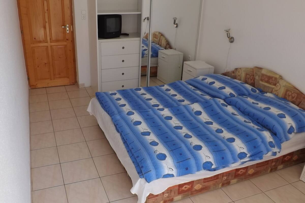 A bedroom with a bed, a wardrobe, a television, and a small cabinet.