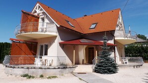 Een twee verdiepingen tellend huis met een rode pannendak, een balkon op de bovenverdieping en een kleine kerstboom in de voortuin.