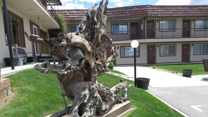 Une grande sculpture naturaliste représentant un arbre, située dans un espace paysager, avec un bâtiment en arrière-plan.