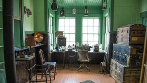 Une pièce aux murs verts, avec un plancher en bois, un bureau orné de machines à écrire anciennes, une chaise et un grand coffre.