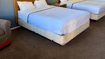 Quarto de hotel com duas camas, cada uma com cabeceira de madeira, roupa de cama branca e um quadro na parede. Há duas luminárias fixadas na parede e uma pequena mesa entre as camas.