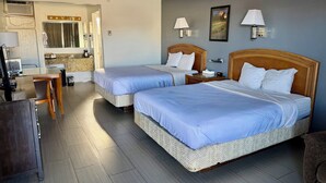 Une chambre d’hôtel avec deux lits, un bureau, une chaise, une télévision et une salle de bain visible à travers une porte ouverte.