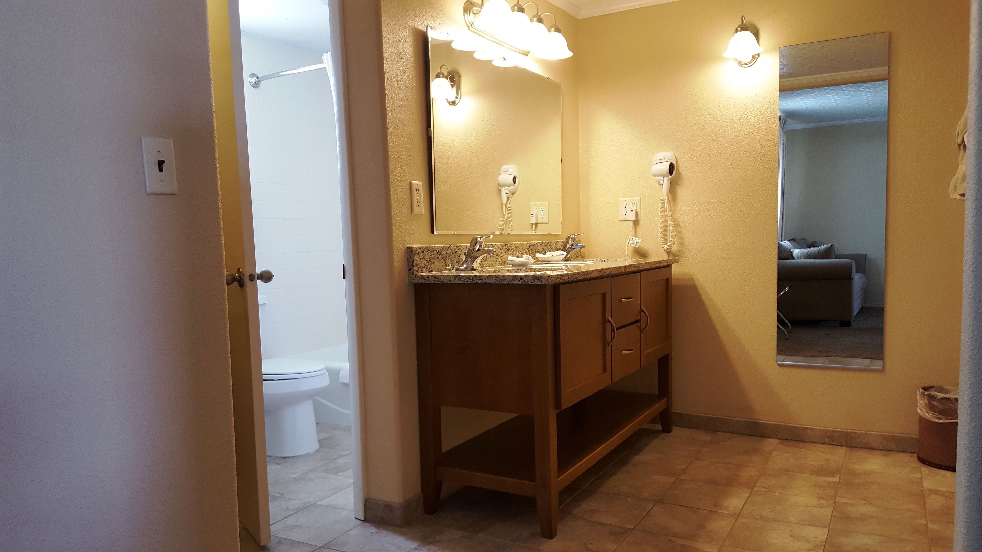 A bathroom with a wooden vanity, a mirror with lights, a shower, and a toilet.