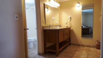 A bathroom with a wooden vanity, a mirror with lights, a shower, and a toilet.