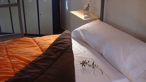 A bed with an orange and brown quilt and white sheets, a small bedside table with a vase of flowers, and a wardrobe in the background. - Albergue Turistico Cornalvo - Hostel (Trujillanos)
