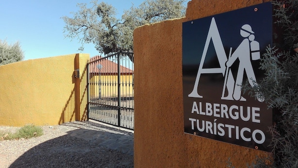 A sign for 'Albergue Turístico' with a gate and a building in the background. - Albergue Turistico Cornalvo - Hostel (Trujillanos)