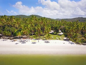 A beach resort with multiple bungalow-style accommodations, a sandy beach, and a backdrop of palm trees and hills. - Pousada Sitio da Prainha (Tamandaré)