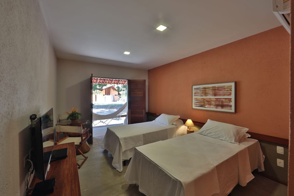 A hotel room with two beds, a desk with a computer, a TV, and a hammock outside the door.