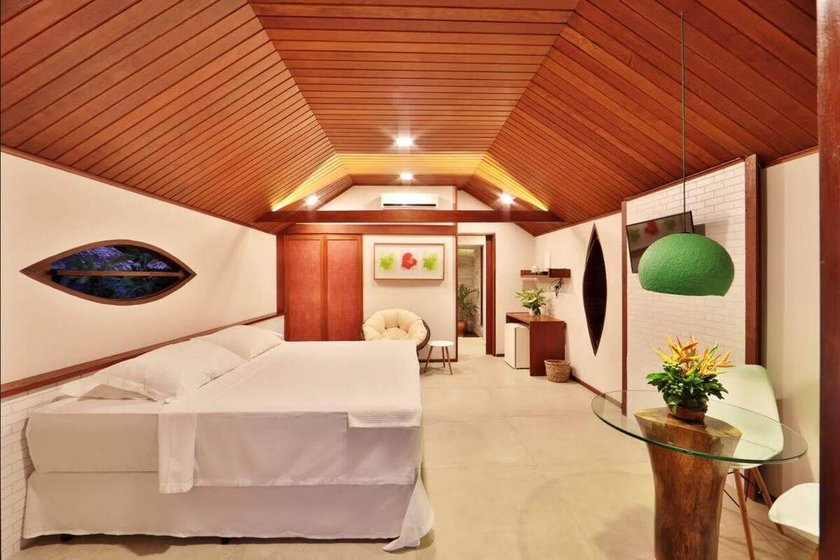 A bedroom with a bed, a round mirror, a small table with a plant, and a chair.