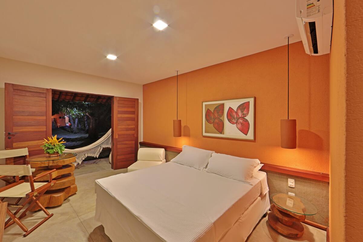 A bedroom with a bed, a hammock, a table with chairs, and a wall-mounted lamp.
